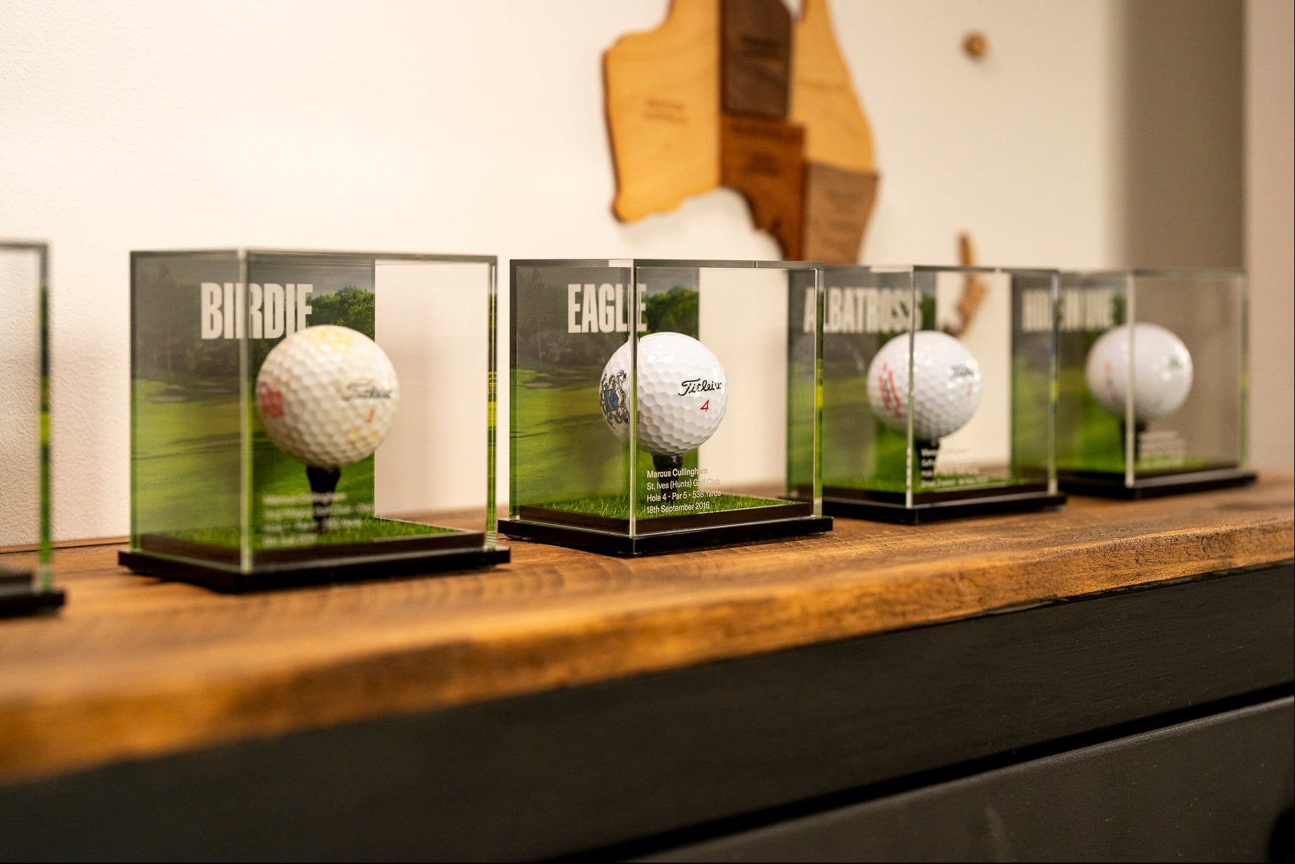 Golf balls in premium display cases on a wooden shelf with a blurred background
